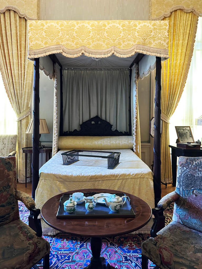 Antique bedroom furniture with yellow damask canopy and drapery panels at The Elms, showcasing Gilded Age Interior Design.