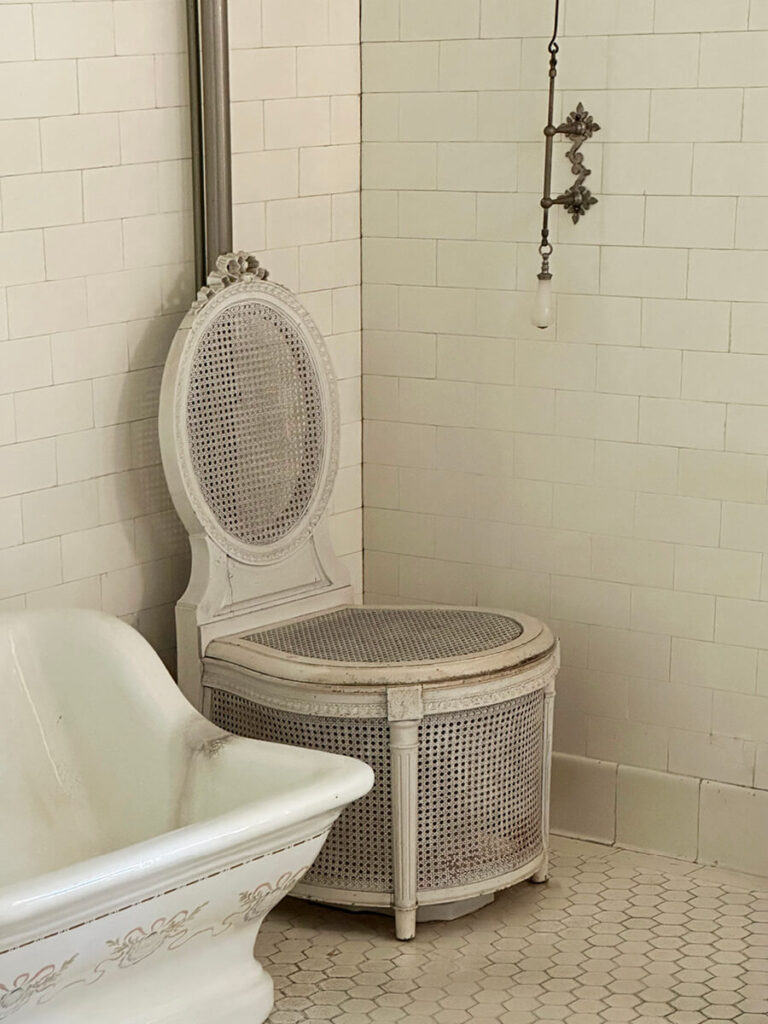 Antique cane furniture beside a vintage water closet in the historic bath design at The Elms in Newport, Rhode Island.