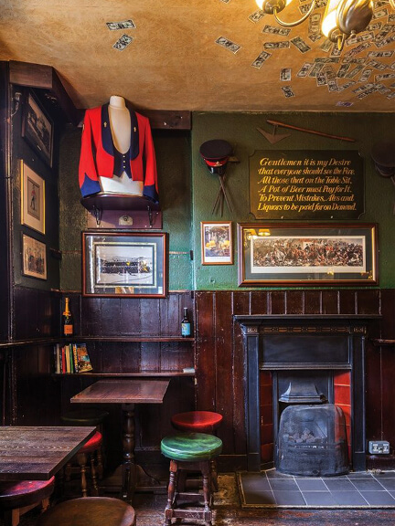 Eat sleep shop London showcases classic interiors at The Grenadier pub with a historic fireplace, green walls, and a ceiling covered in money.