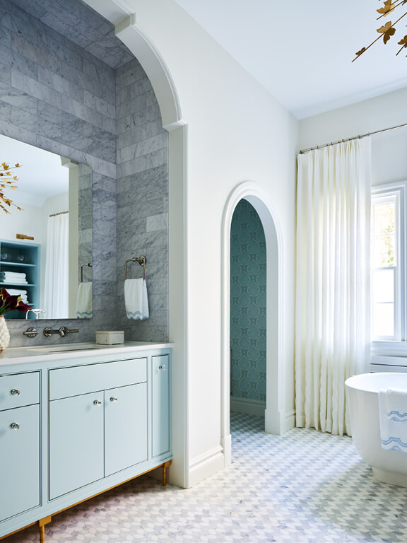 Blue cabinet vanity in an alcove with marble tile, gilded light fixtures, and leaf-motif mosaic flooring in a luxury Milton bathroom
