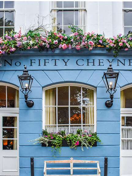 London restaurant design at No 50 Cheyne features a blue and white historic building with overflowing flowers and traditional light fixtures.