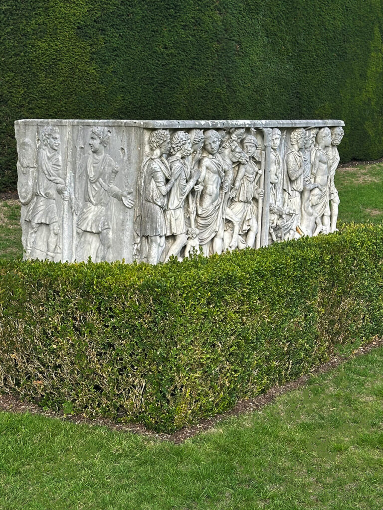 Ancient marble sarcophagi displayed in the forecourt of Cliveden House, surrounded by stone paving and manicured garden walls.