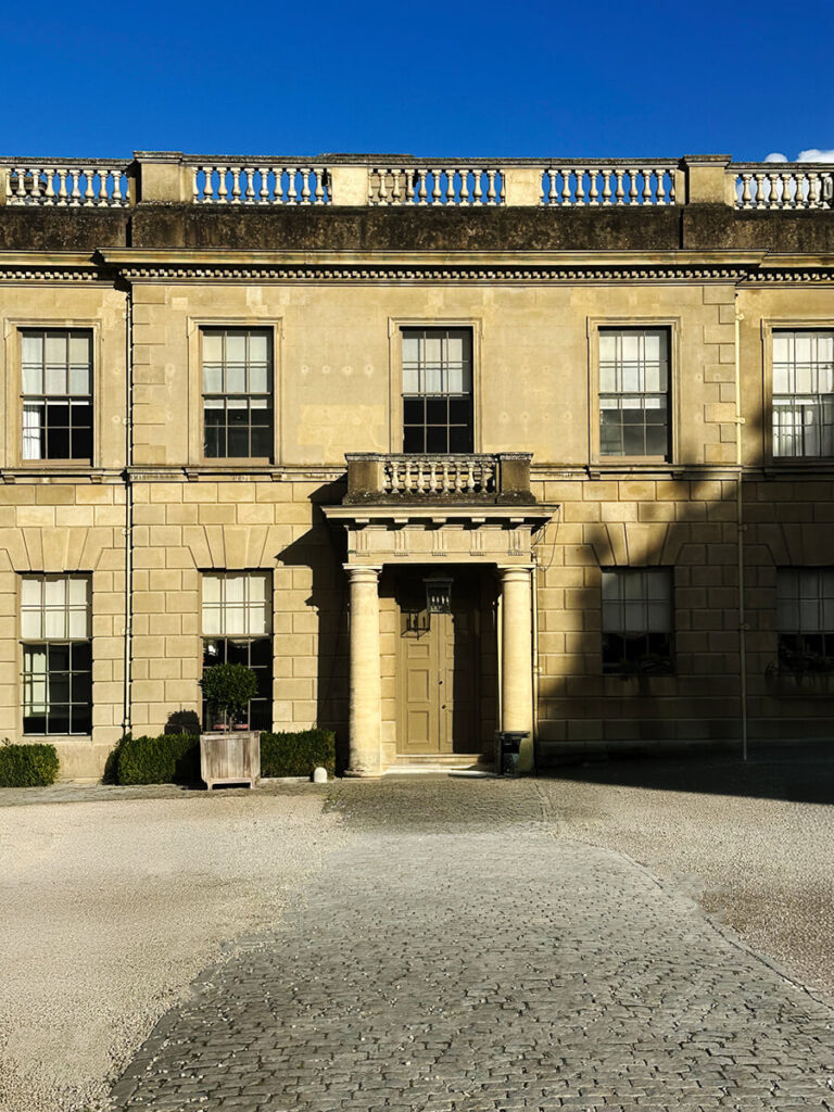 Grand entry and front door of a historic English estate, featuring stone columns, carved details, and symmetrical architectural design.