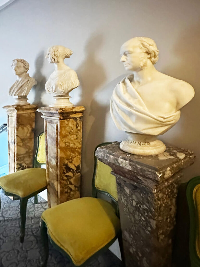 Grecian and Roman busts on stone pedestals with green Queen Anne chairs in English manor interior design.