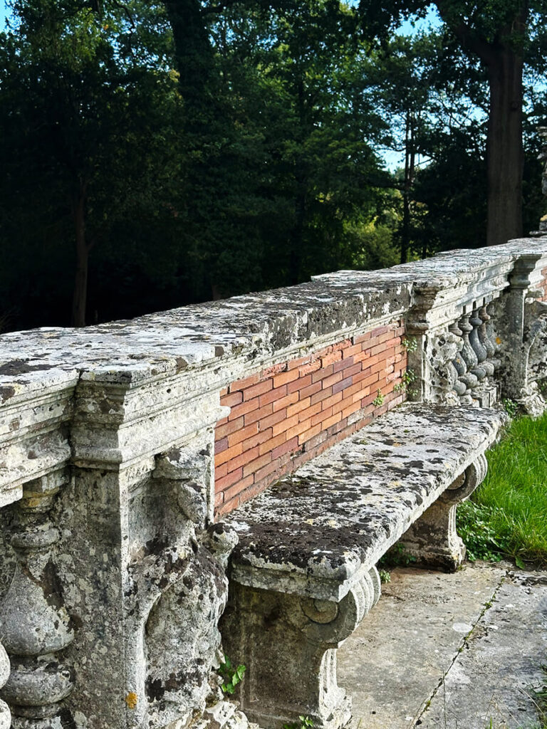 Stone bench and brick garden details within a historic English garden, surrounded by ivy, aged walls, and sculptural plantings.