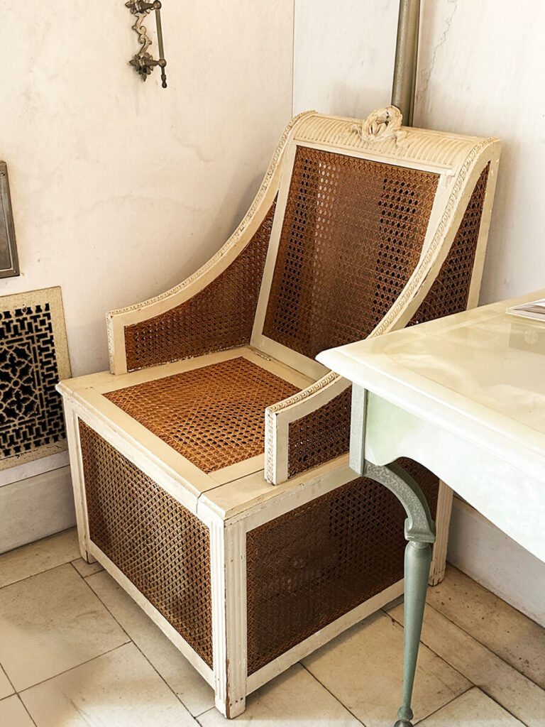 Antique cane furniture in the historic bathroom at The Elms in Newport, combining natural materials with refined early 20th-century design.