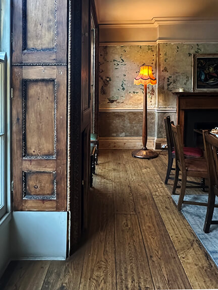 Aged wood paneling with layered paint, fringed lamp, and vintage furniture in a historic Belgravia pub interior.