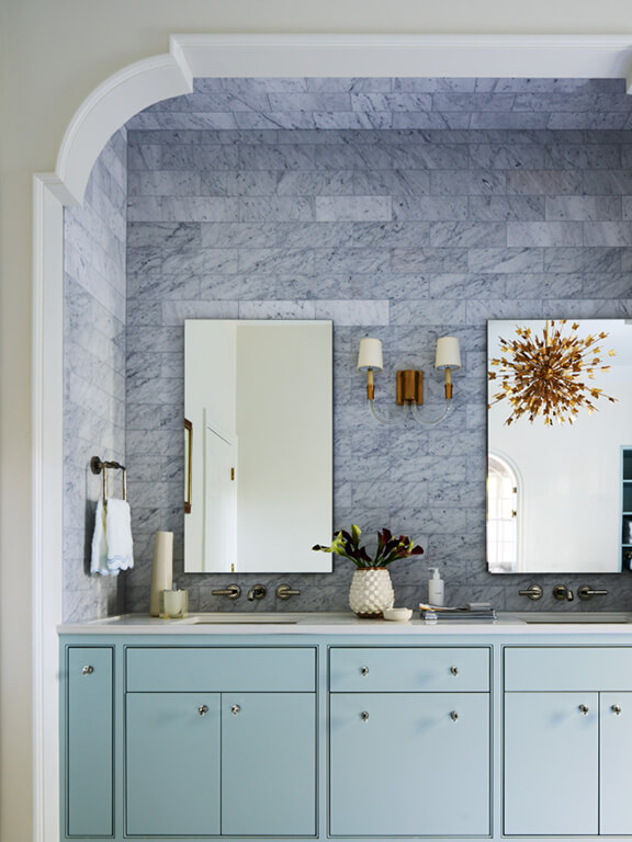 Light blue cabinet vanity with brass light fixture, white marble tile backsplash, and wall-mounted Kallista faucets in a Boston primary bathroom