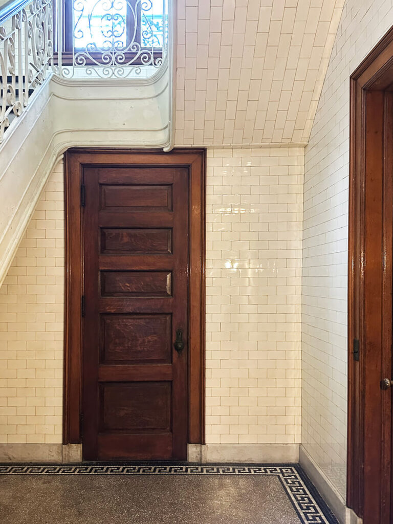 Natural wood door and floor-to-ceiling wall tile at a historic staircase in a New England mansion, showcasing classic architectural detail.