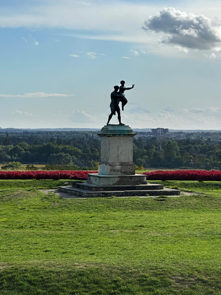 Pluto and Proserpina bronze sculpture in the gardens of Cliveden House, surrounded by manicured hedges and seasonal blooms.