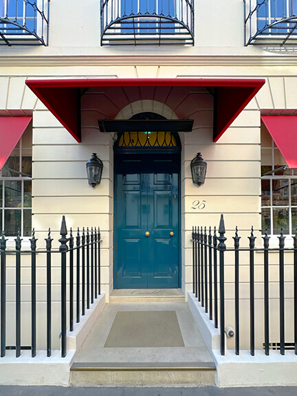 Blue lacquered front door and red awning at Oswald’s private club and restaurant in London with cool interior design appeal.