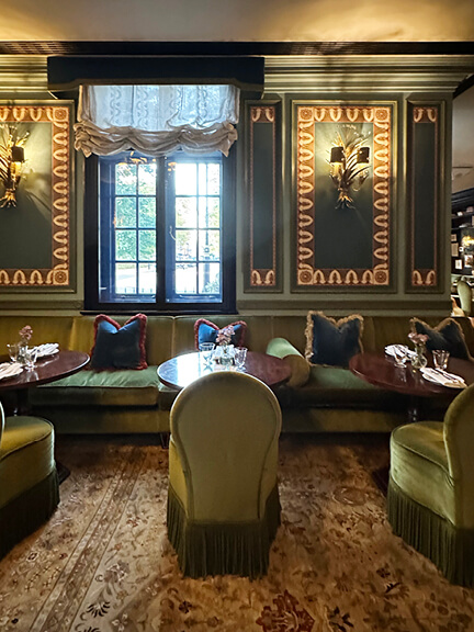 Green slipper chairs with fringe, painted wall panels, and Austrian shades at The Twenty Two luxury hotel in London.