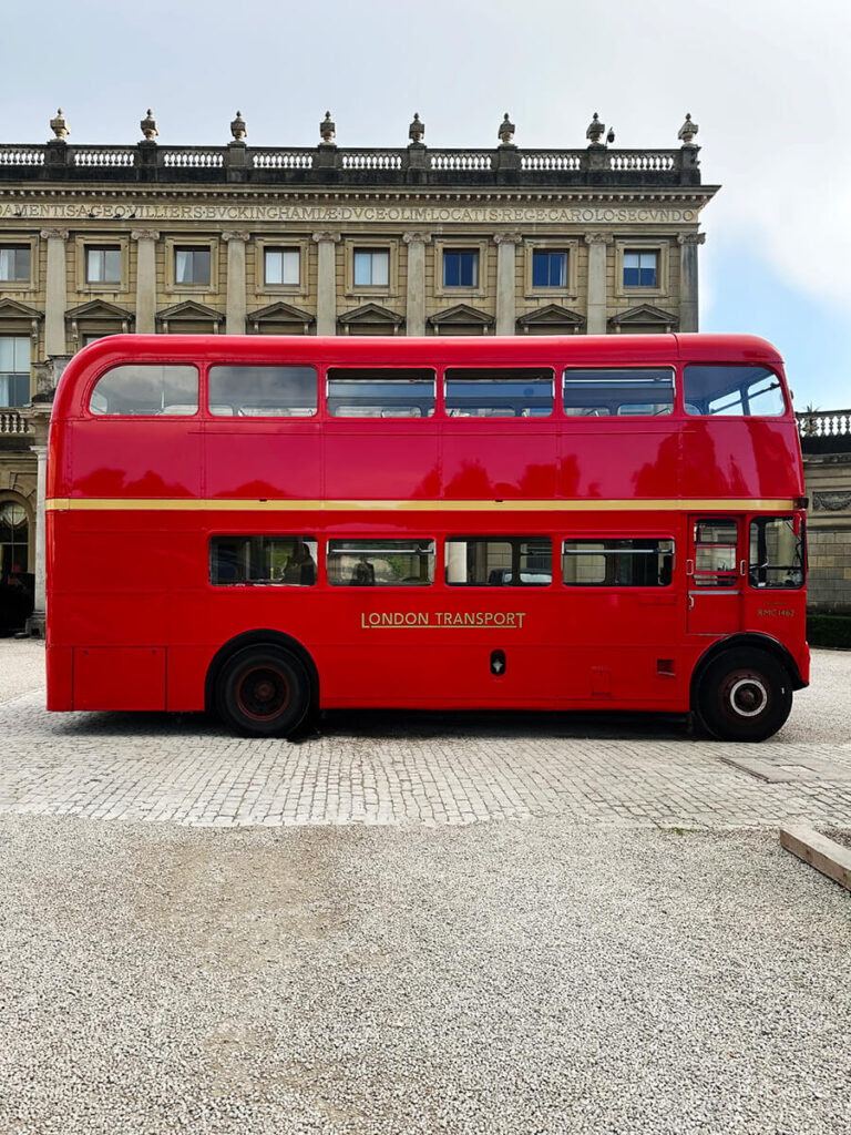 Historic English Estate Design captured with a vintage red bus parked before the grand facade of Cliveden House in Buckinghamshire.