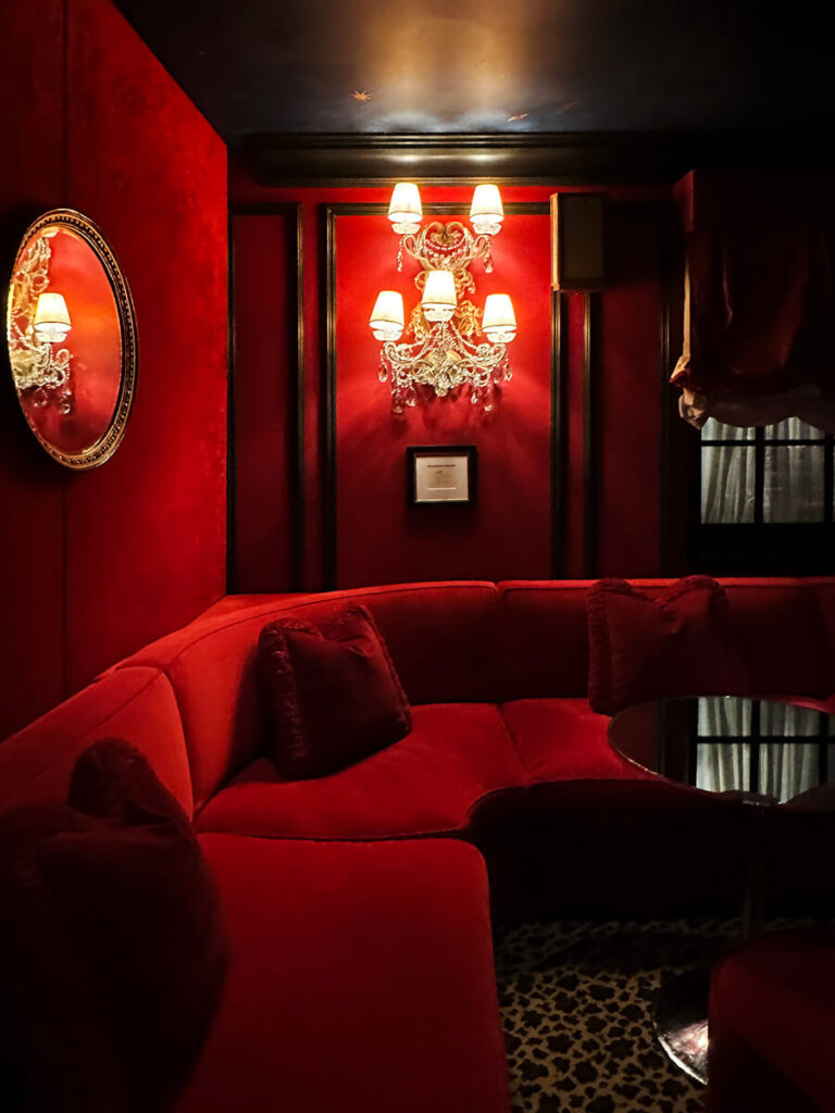 Red velvet sofa in a London club-style room at The Twenty Two in Mayfair, with red lacquered walls and vintage lighting.