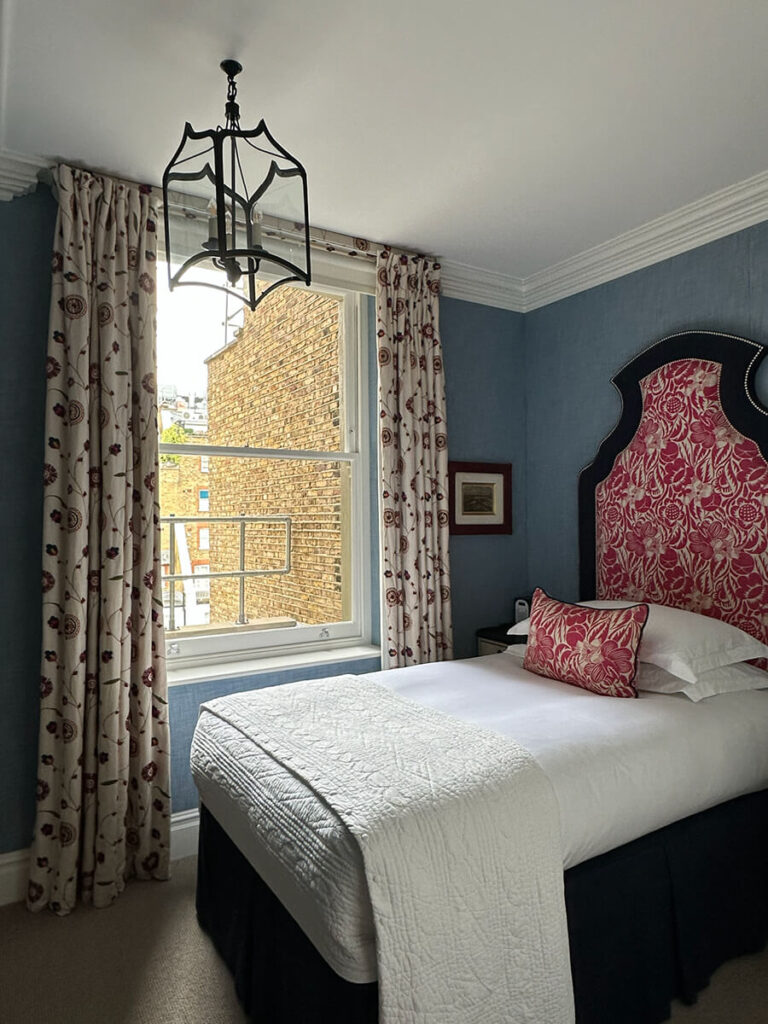 Eat sleep shop London features blue wallpaper, a red floral headboard, and a vintage lantern at Kit Kemp’s Knightsbridge Hotel.