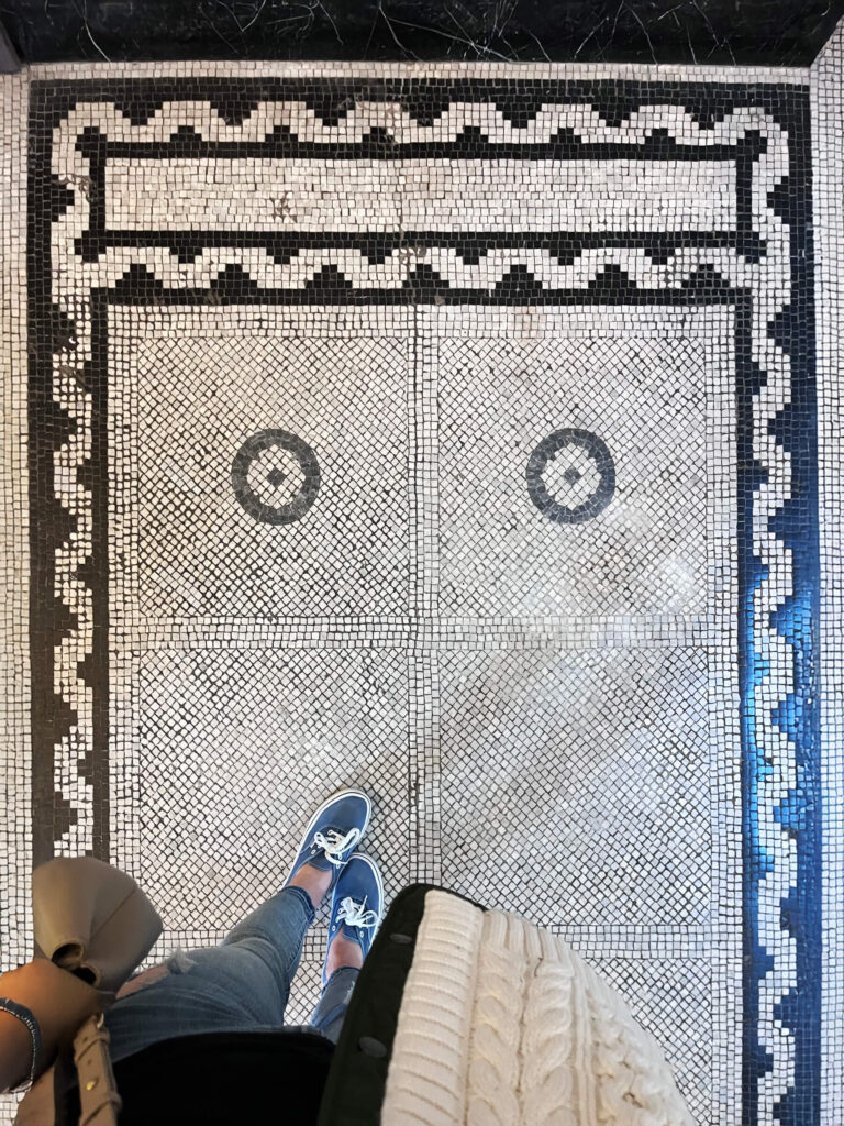 Historic tiles in old building appear as black and white mosaic flooring inside the Victoria and Albert Museum during a Boston interior designer’s visit to London.
