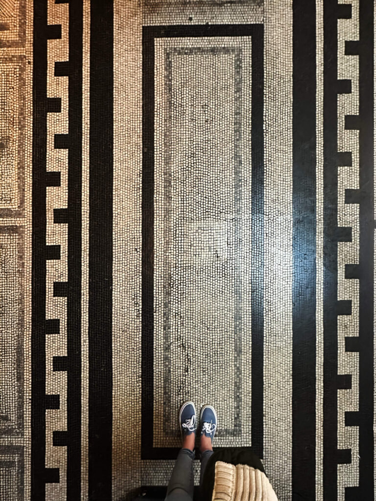 Victorian tile patterns appear in a black and white Greek fret mosaic floor inside the historic Victoria and Albert Museum in London.