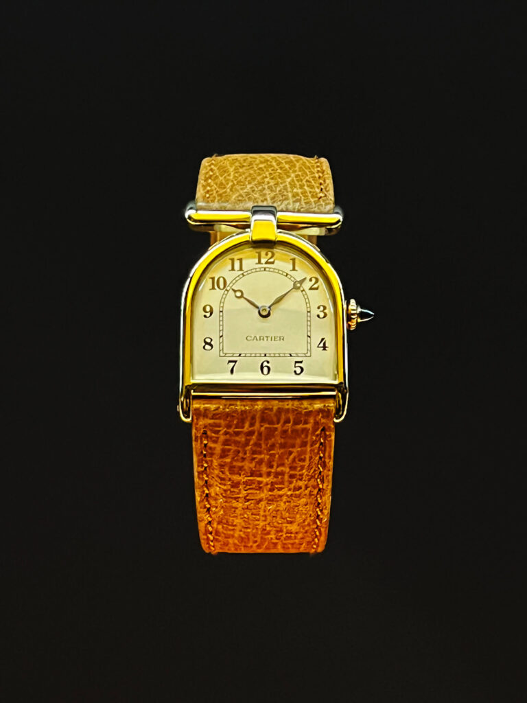 A 1923 Cartier cloche-shaped watch with sapphire accents, yellow and rose gold details, and a leather strap from the Cartier Jewelry Exhibit.