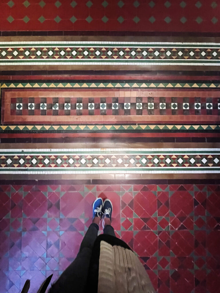 Colorful encaustic tiles in red, green, and camel appear on the floor of a historic London museum building.