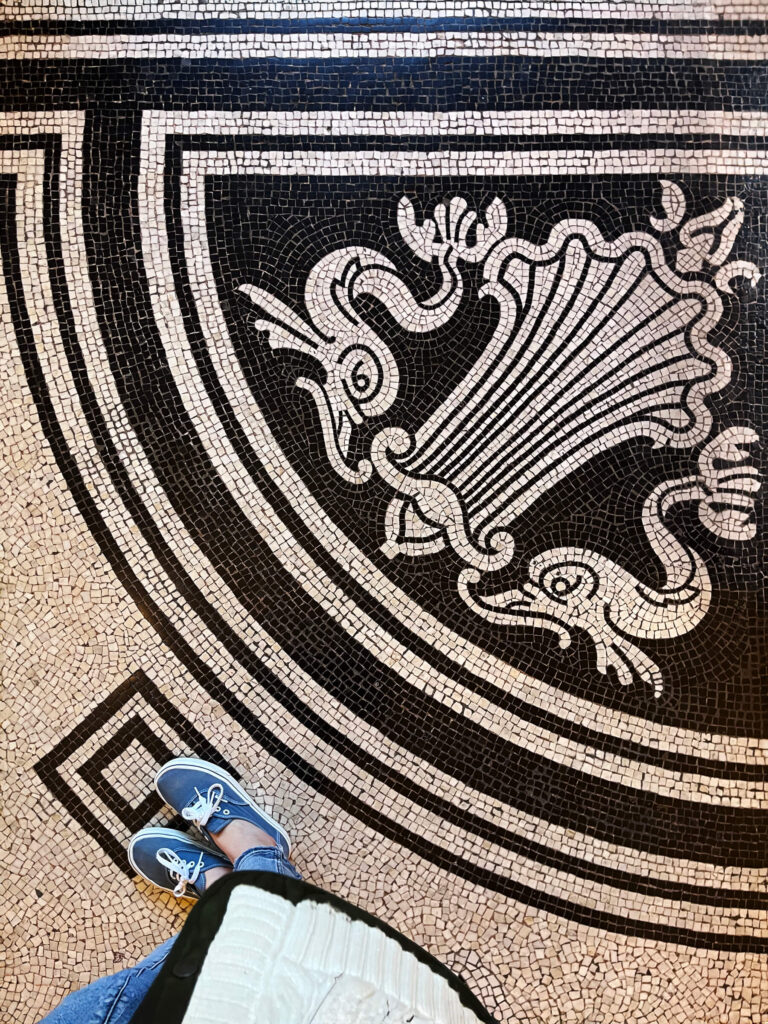 A black and white heraldic-style mosaic tile pattern appears on the floor of a historic Victorian building in London.
