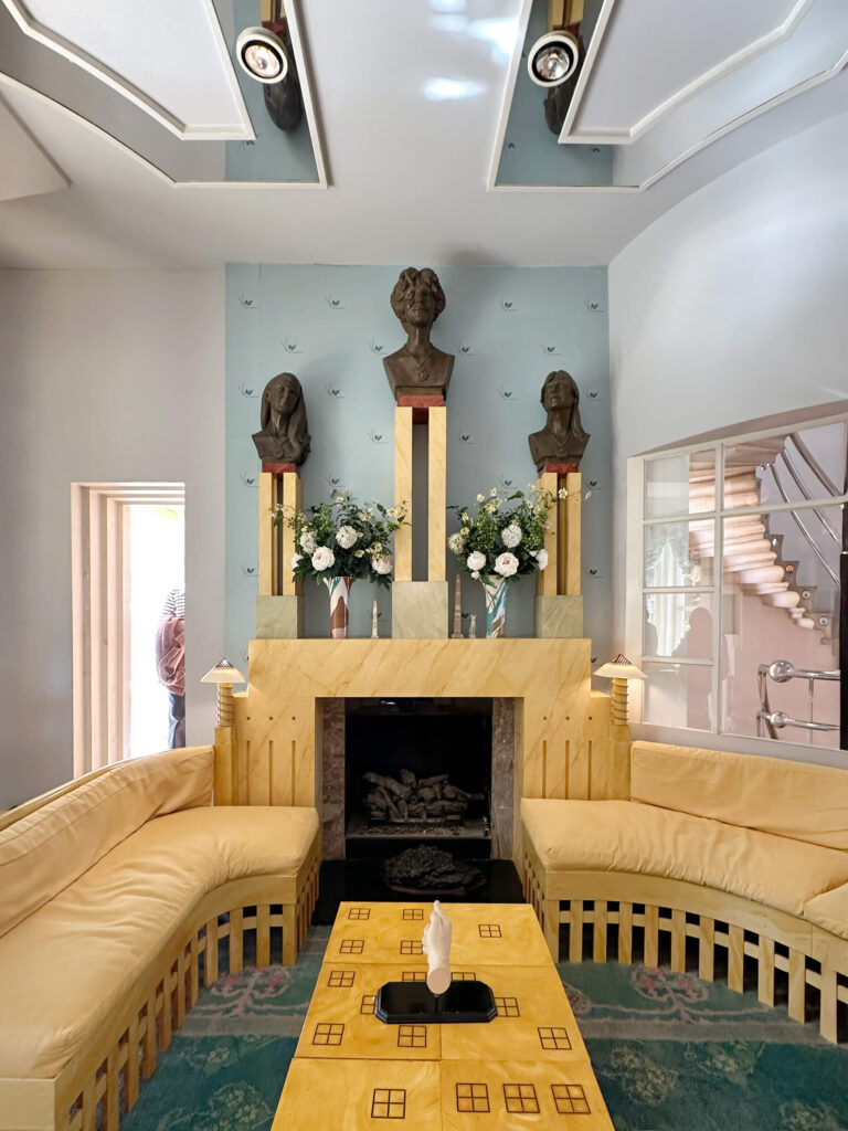 Light yellow marble fireplace with curved custom sofas, light blue walls, and bronze busts