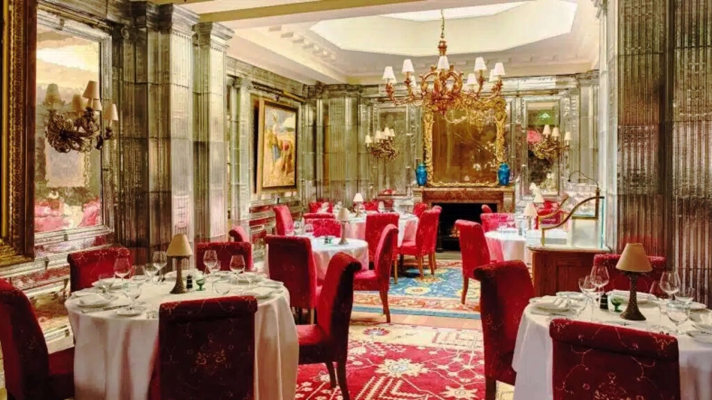 Oswald’s London interiors with silver textured glass panels and traditional red velvet chairs, a look tied to expressive London restaurant design.