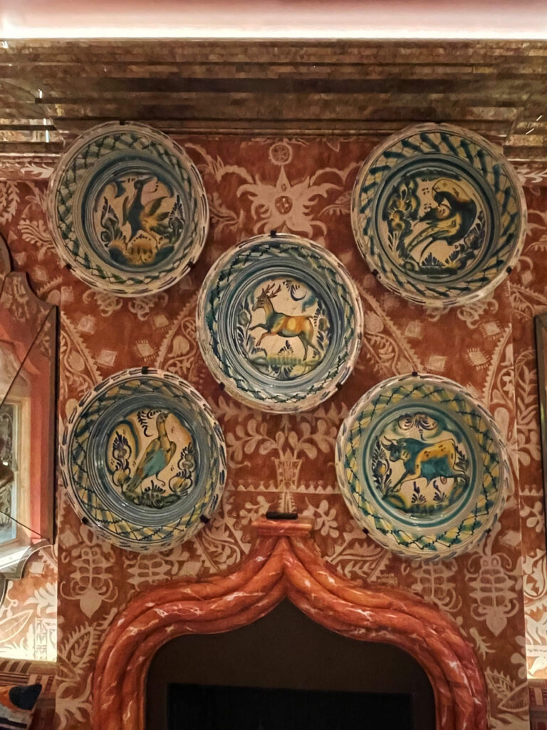 Colorful vintage ceramics and pink wallpaper at a pink marble fireplace show cool interior design at private London restaurant Oswald’s.