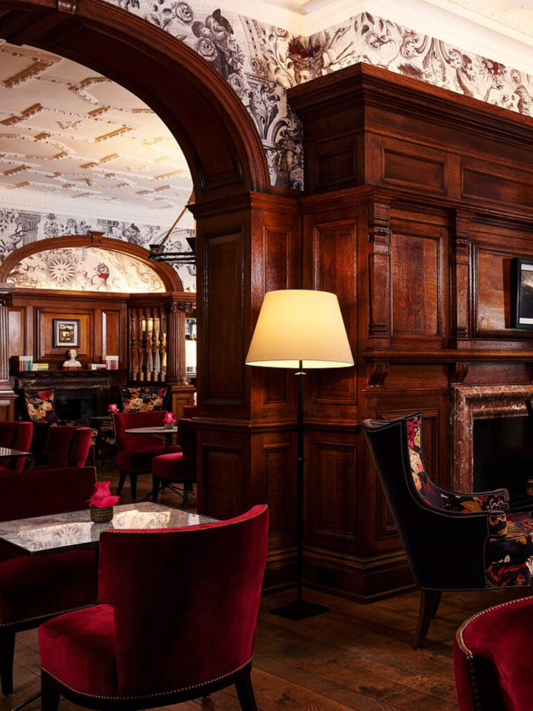 Red velvet chairs London restaurant with wallpaper, wood work, and an ornate ceiling, shown in layered London restaurant design.