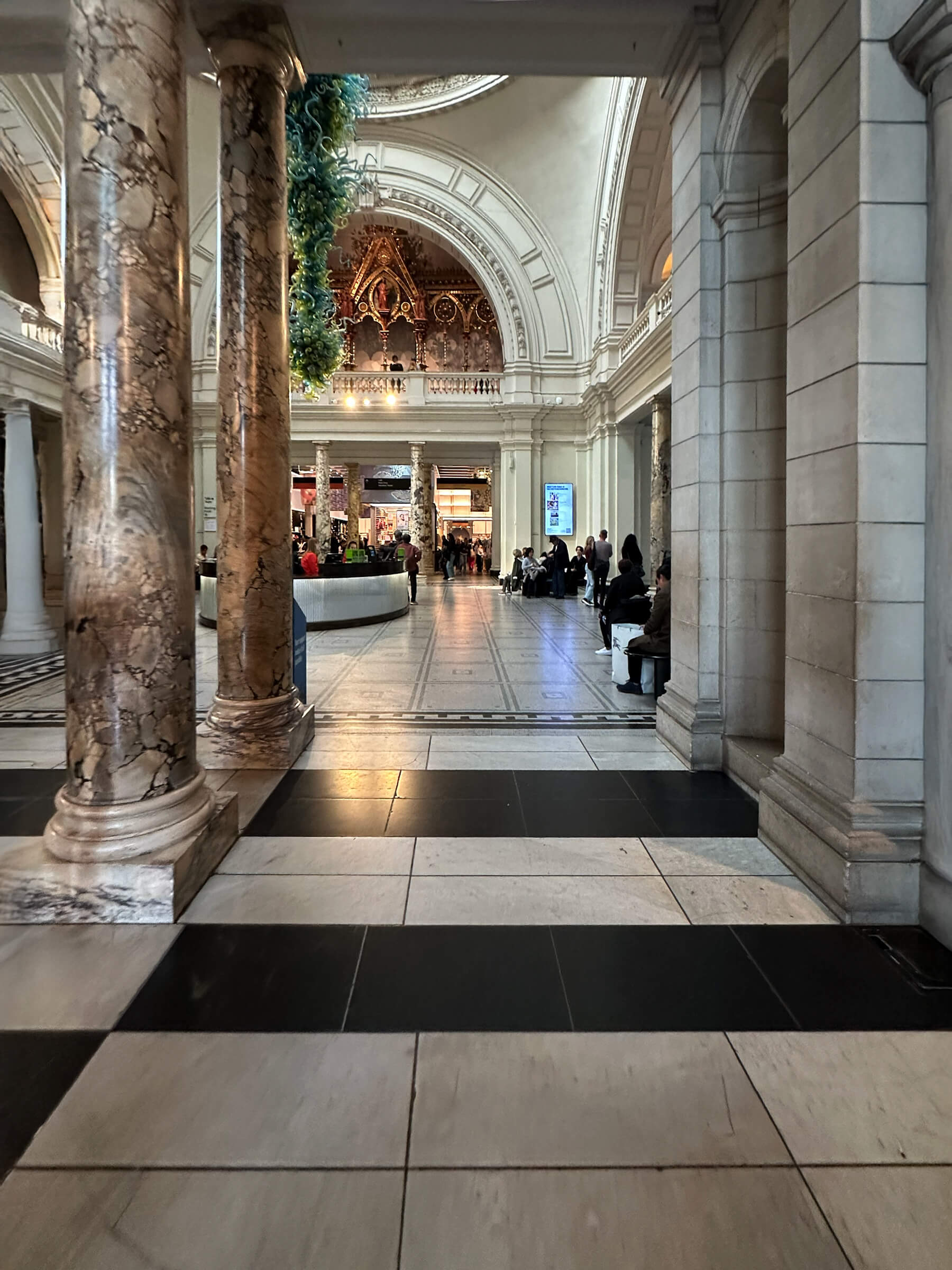 Black and white marble pavers appear as large stone tiles in a historic London museum, framed by marble columns, a classic dome, and grand arches.