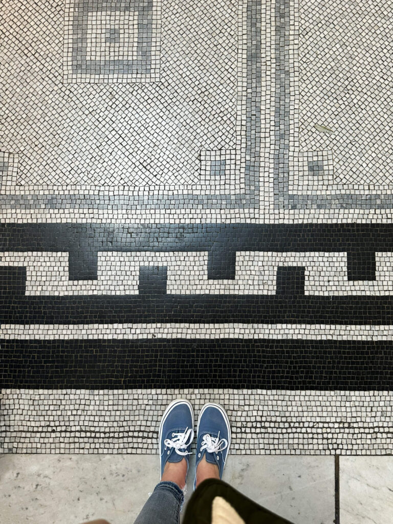 Black geometric trim tiles frame white and light grey field tiles with square and angular shapes inside a historic London museum.