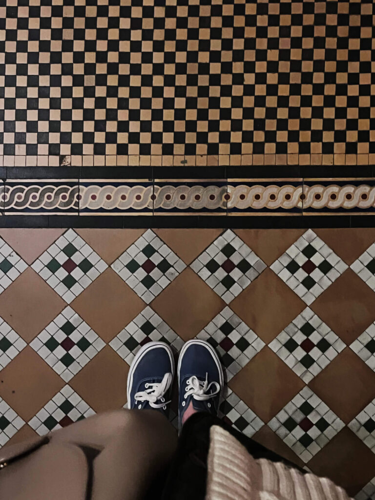 Victorian tile patterns appear in brown, black, and white mosaic flooring inside the historic Victoria and Albert Museum in London.