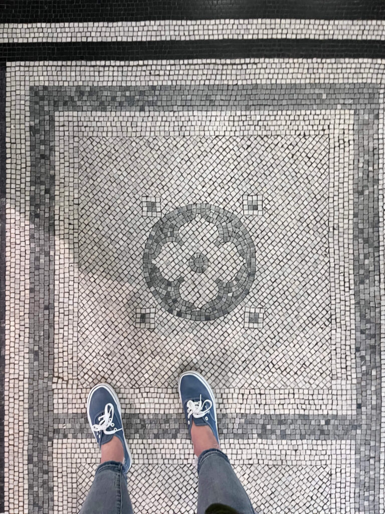 Light grey and white mosaic tile flooring with a black border appears as original historic flooring inside a London museum.