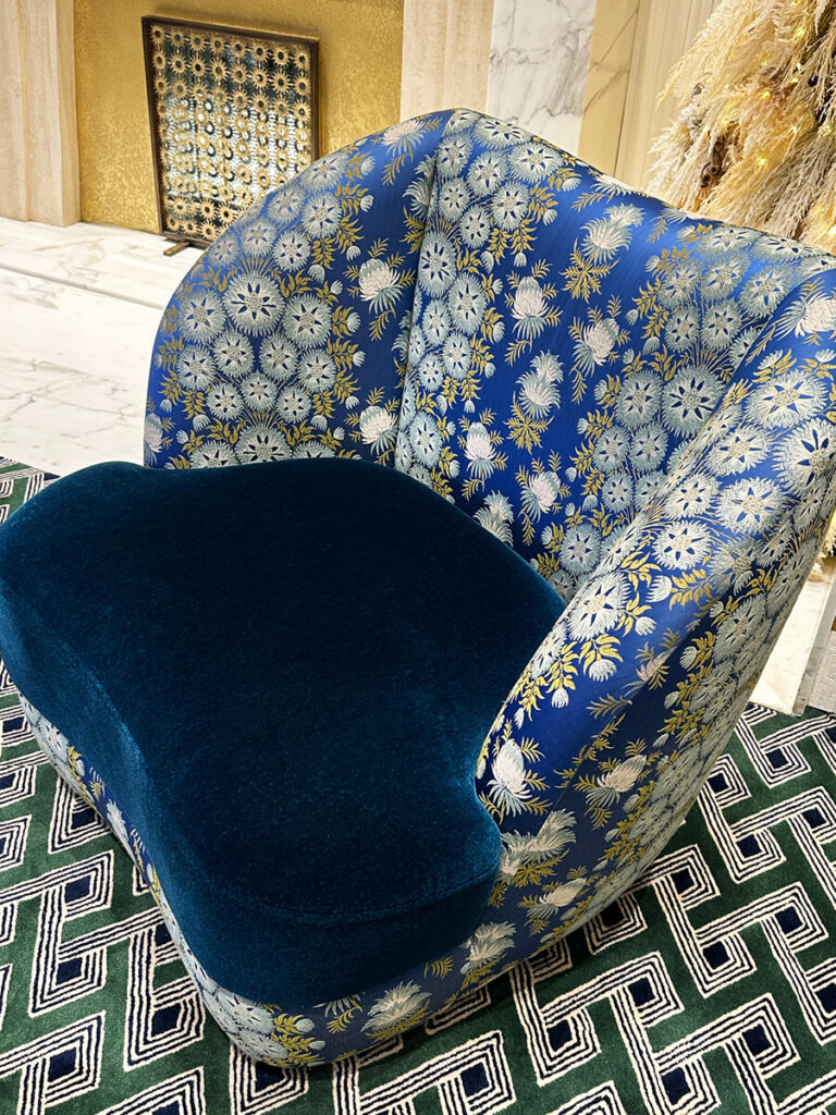 Cartier Mansion New York blue velvet upholstered chair with gold and green fabric beside a brass table on soft gold carpet