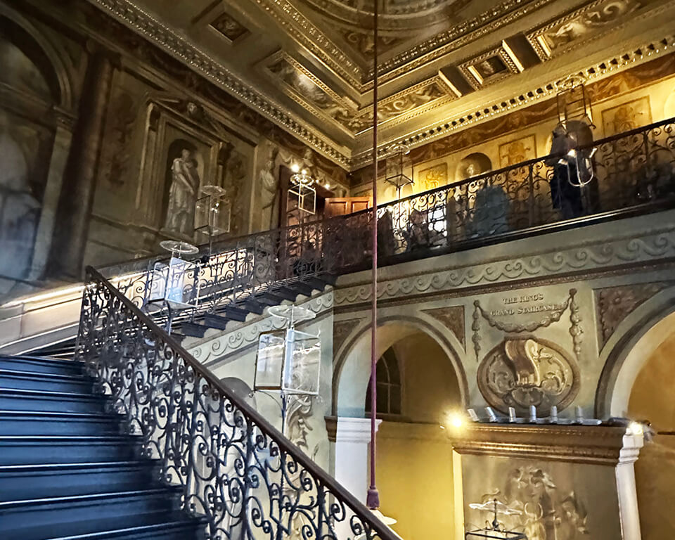 Kensington Palace Interiors showcasing the grand staircase with painted walls, iron balustrade, and historic detailing.