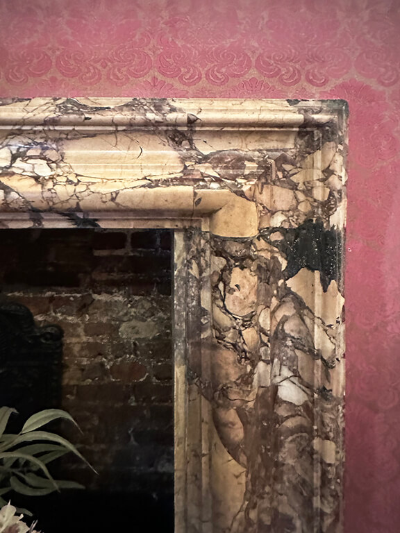 Marble fireplace set against soft pink wallpaper in a historic interior at Kensington Palace.