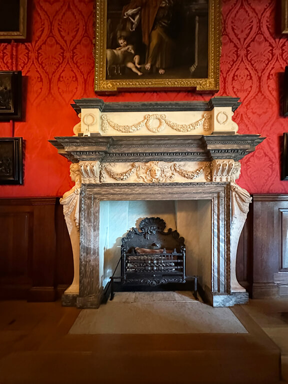 Kensington Palace Interiors featuring an ornate marble fireplace set against red damask walls in a formal historic room.