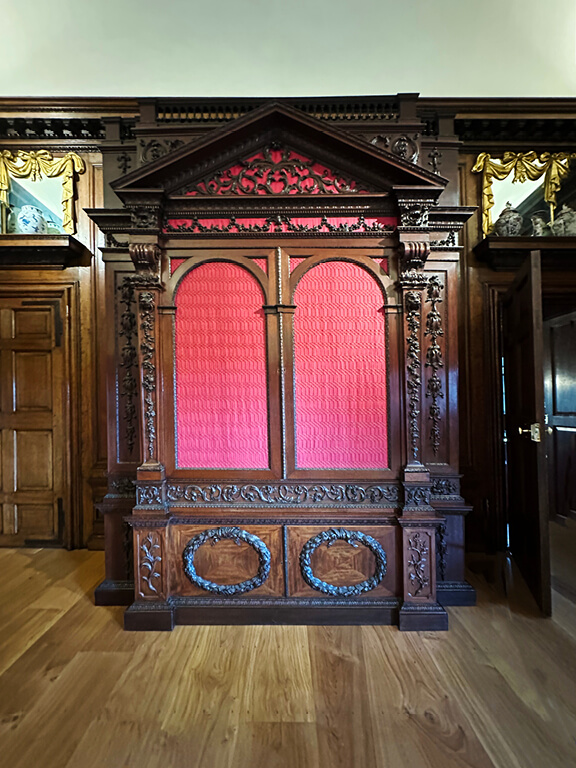 Kensington Palace Interiors featuring ornate wood paneling paired with rich red fabric in a formal historic room.