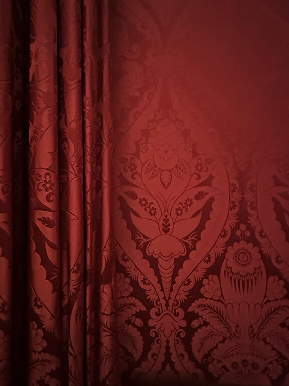 Red damask fabric defining a formal British interior inside Kensington Palace in London.