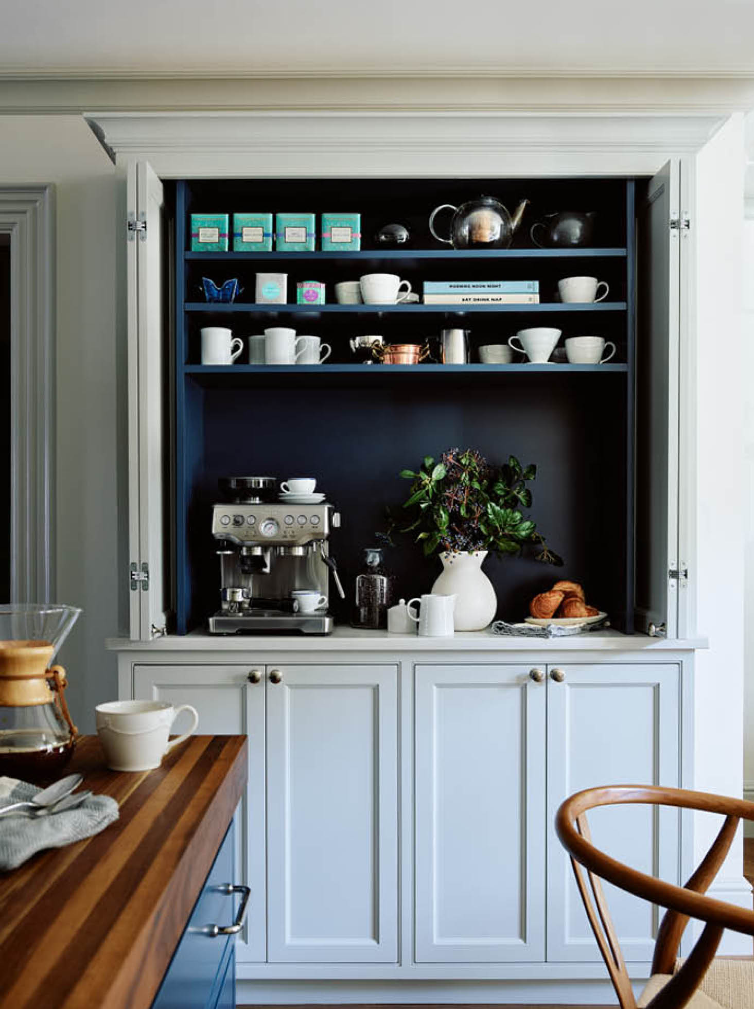 Custom pantry unit with bifold doors that pocket inside, navy-painted interior with space for an espresso machine, tea kettle, mugs, and more.