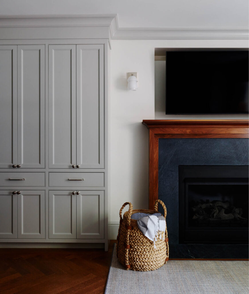 The new custom fireplace features a soapstone and walnut surround, complemented by custom gray cabinets at the edge of the kitchen.