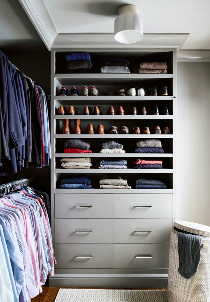 The primary closet in a historic brownstone renovation features custom light gray cabinets, open shelves, double hanging space, and drawers for organized storage.