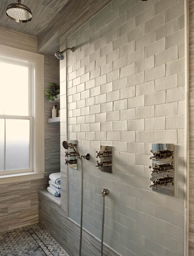 
The primary bathroom in a historic brownstone renovation features polished nickel British fixtures, custom-colored wall tile framed by stone, and mosaic tile flooring designed by Sarah Scales.