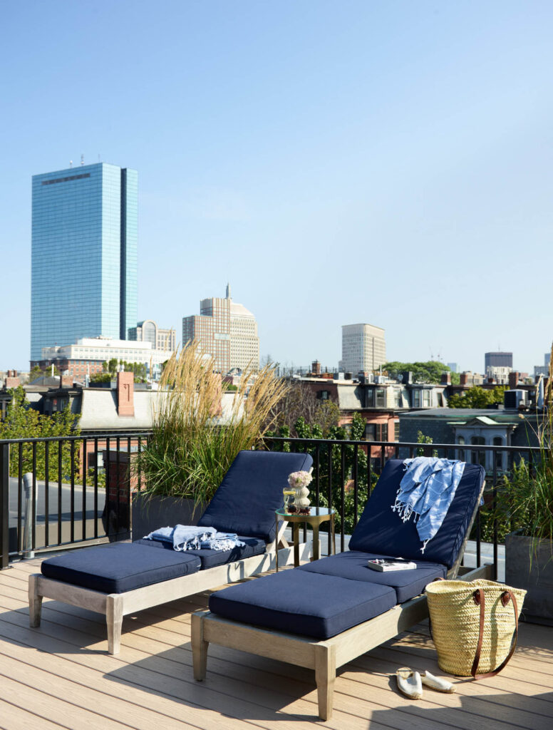 Chaise lounge chairs on the roof deck of the Boston brownstone offer a view of the city, including the Prudential building in the distance, designed by Boston interior designer.