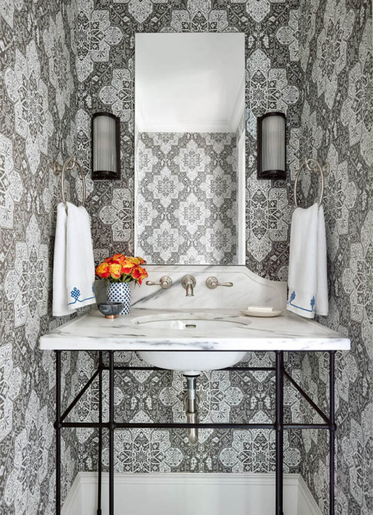 Powder room with Thibaut wallpaper, marble console sink, wrought iron base, wall-mounted faucet, simple mirror, and oil-rubbed bronze sconces.