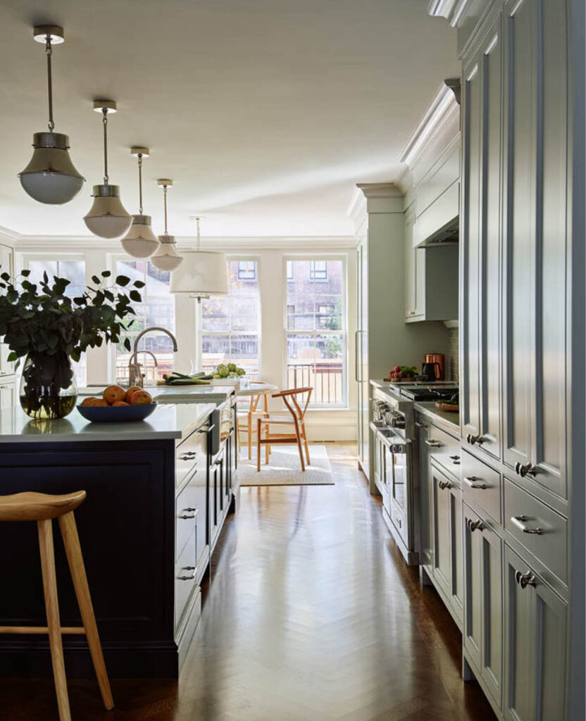 Light grey custom pantry cabinets in a historic brownstone renovation, featuring a Farrow & Ball Hague Blue island, herringbone flooring, polished nickel pendants, and mid-century modern furniture.