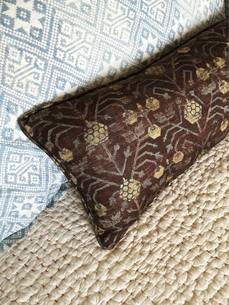 Natural fiber bedspread with blue patterned shams and a purple linen pillow in the primary bedroom of a Vermont interior design project. 