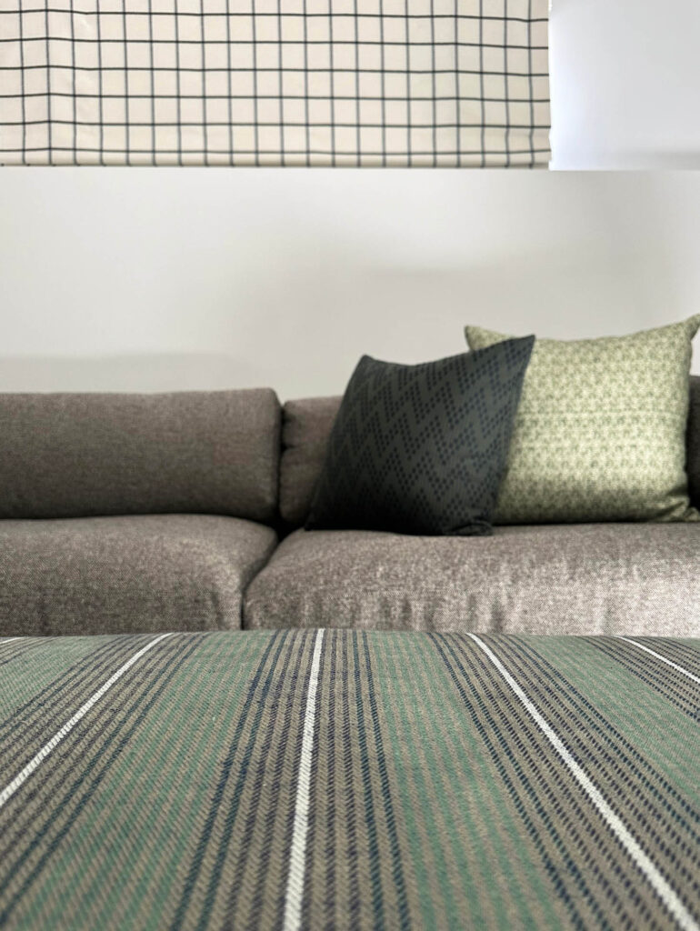 Custom dark green striped ottoman in Zak & Fox fabric with throw pillows and plaid shades in the basement media room designed by Sarah Scales.