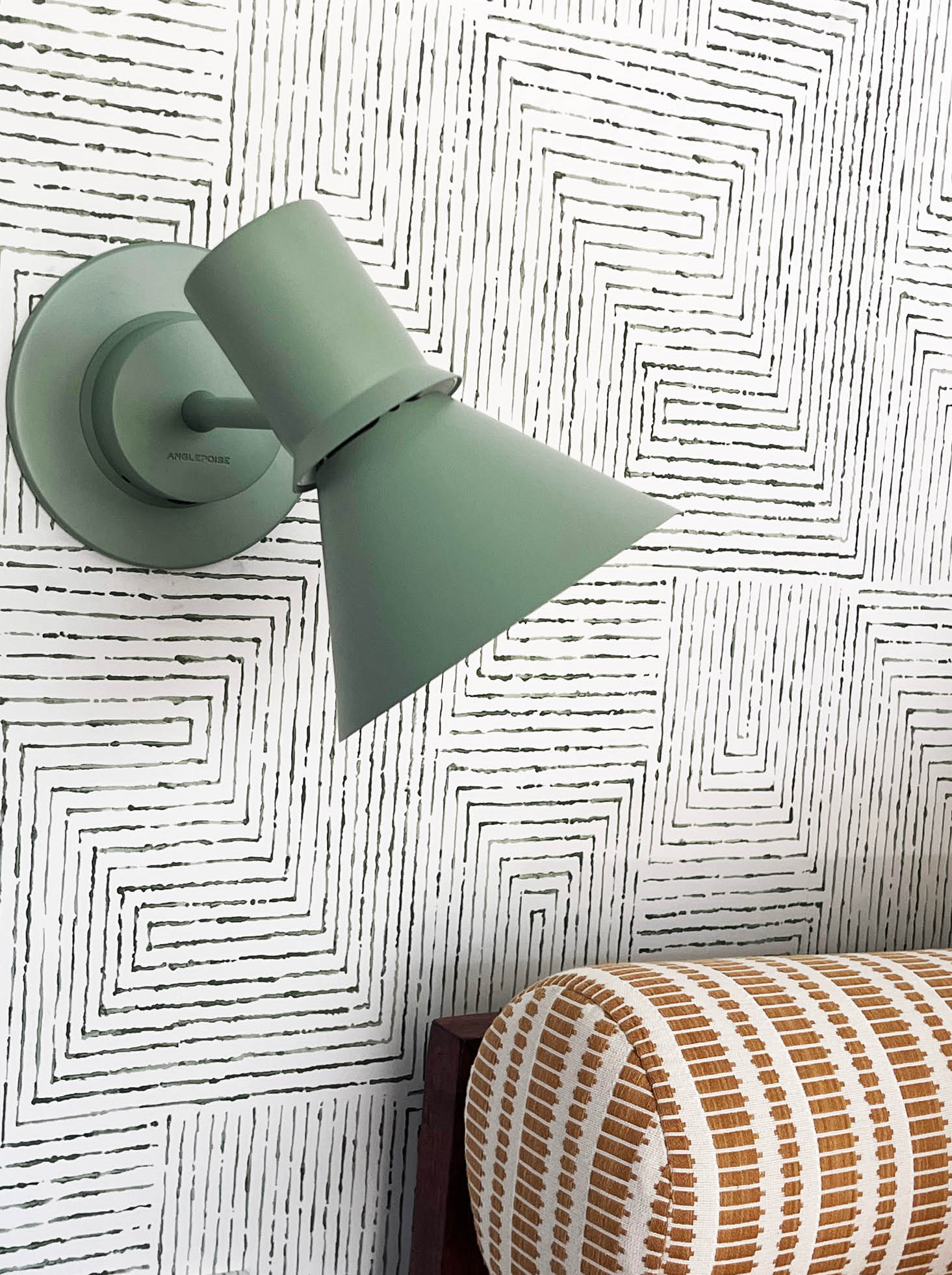 The basement bunk room features an Angelpoise light green sconce against Kravet green and white geometric wallpaper, with yellow upholstery adding contrast.