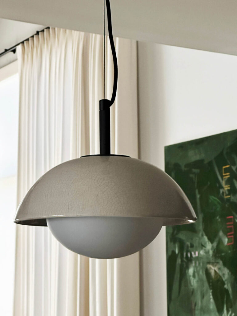 Kitchen pendant light with crackled ceramic feature, white drapery, and dark green canvas in the Vermont mountain home.