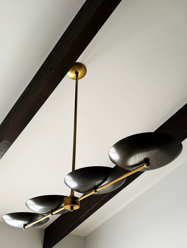 Brass and black metal dining room light from Arteriors with exposed wood beams in Vermont mountain home.